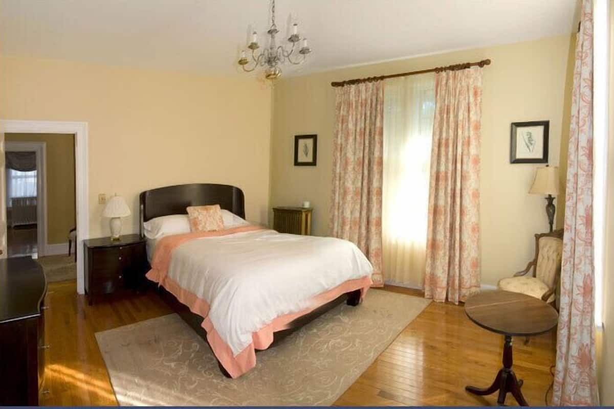 Un dormitorio con una cama, una mesita de noche, una silla, una mesa y una araña.