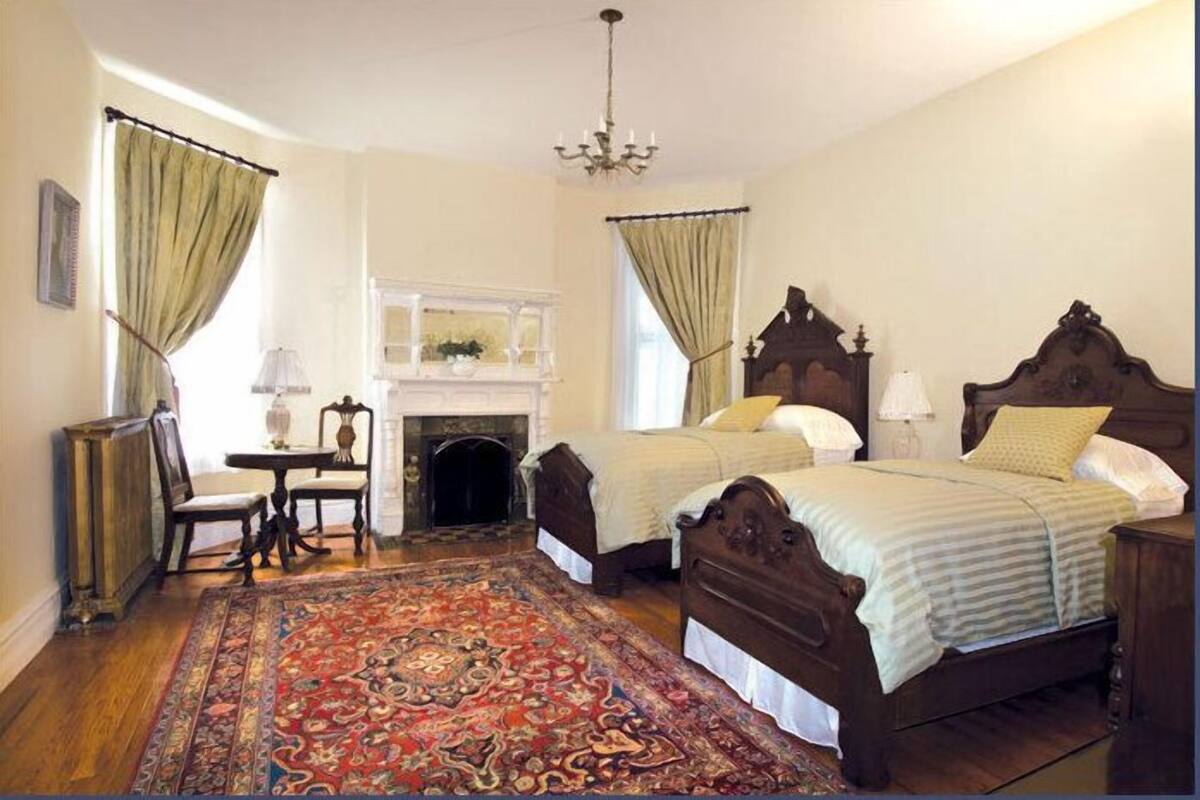 Un dormitorio tradicional con dos camas de madera, una chimenea, un candelabro y una alfombra estampada.