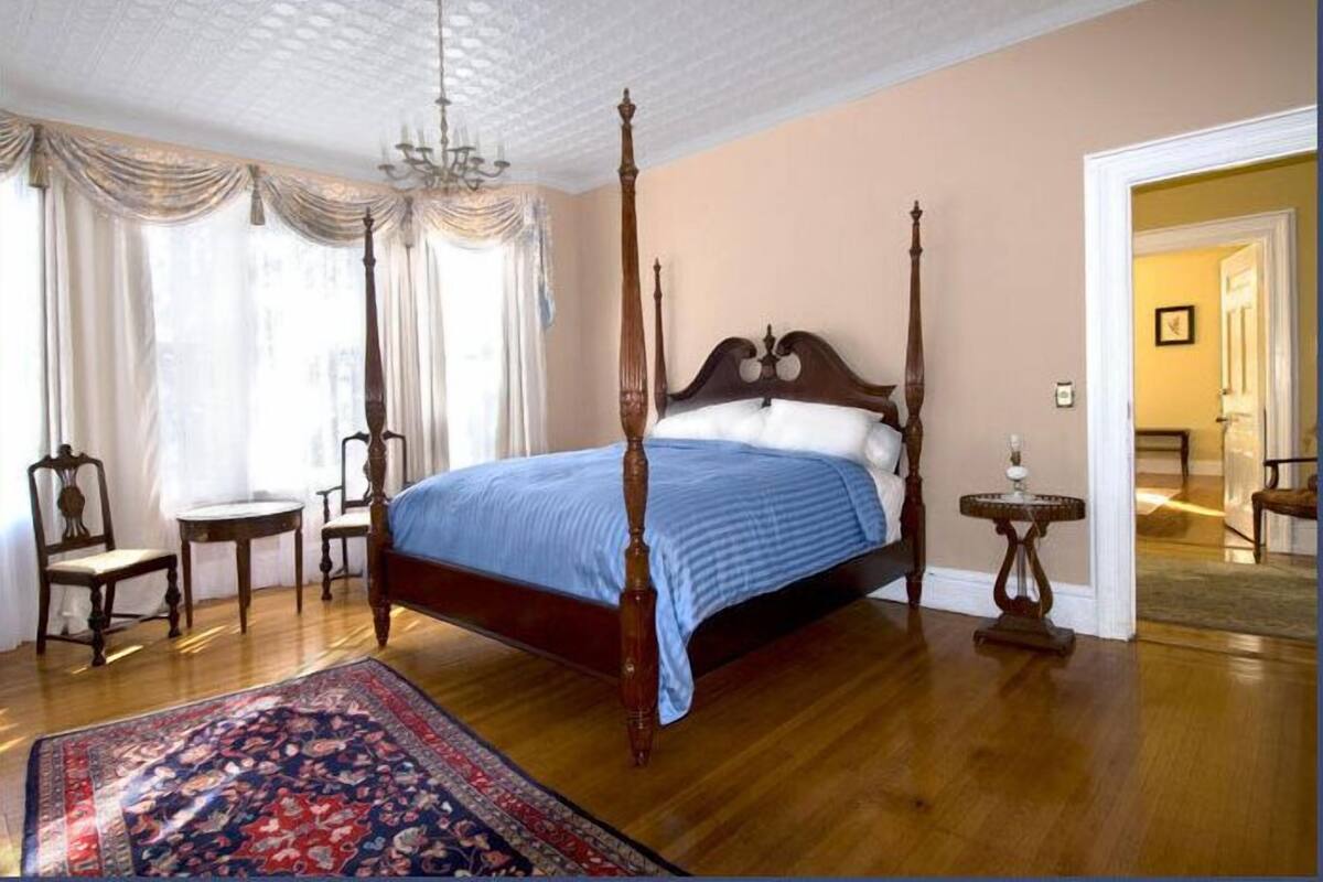 Una cama con dosel con un edredón azul, piso de madera y un candelabro tradicional.