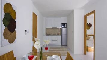 A modern dining area with a wooden table set for two, white plates, and a vase with white flowers.