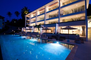 A multi-story hotel with a swimming pool, outdoor seating, and palm trees.