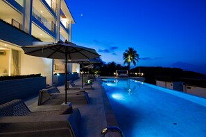 A poolside area with lounge chairs and umbrellas, a pool, and a building with balconies.