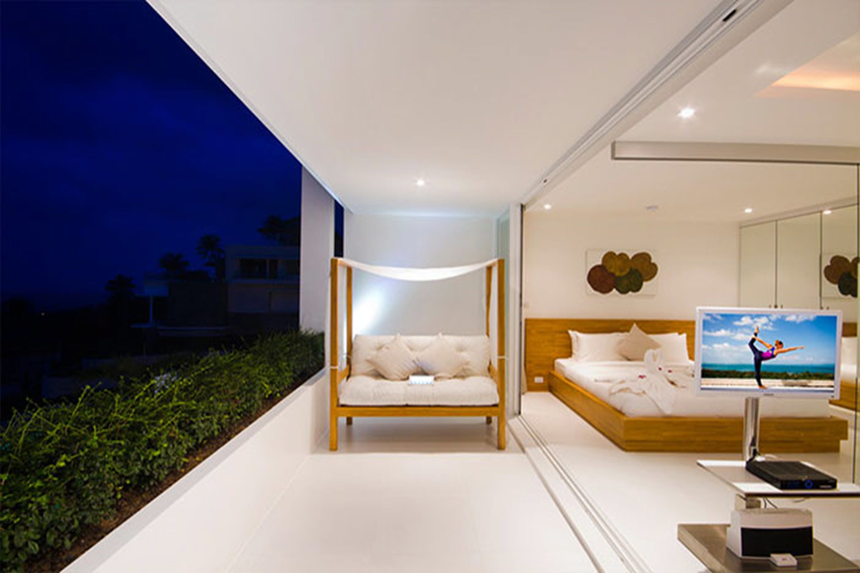 A modern bedroom with a large bed, a bedside TV, and a balcony with plants.