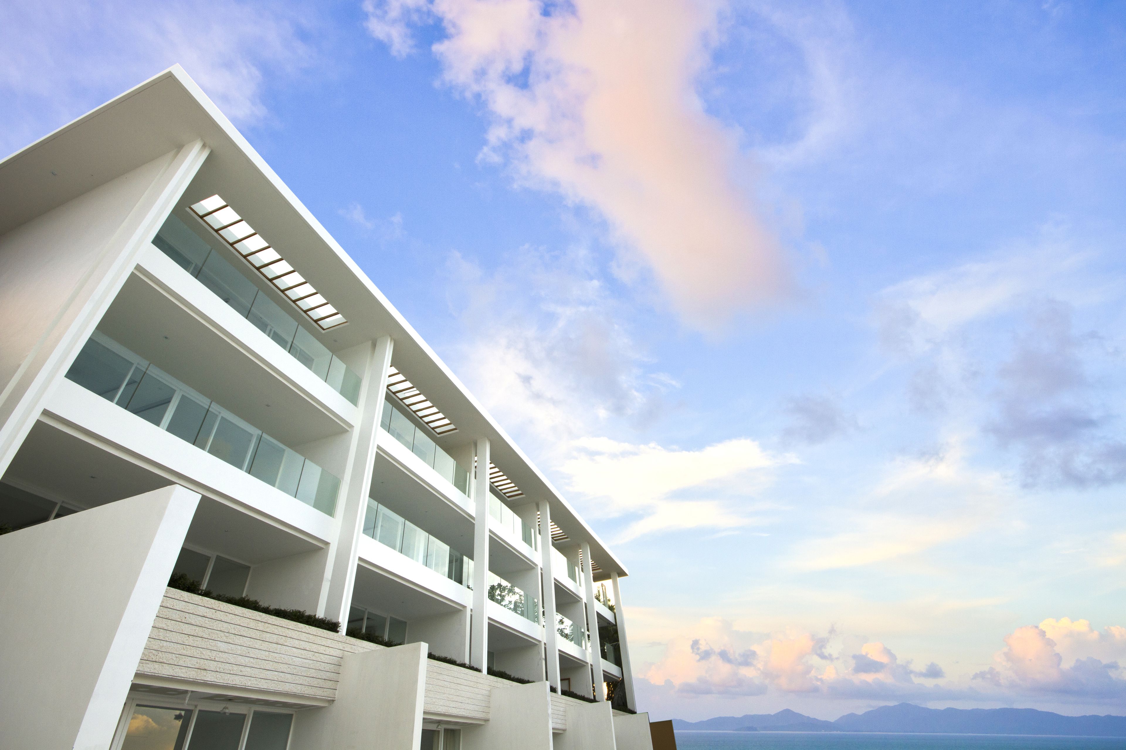 A modern multi-story hotel with balconies and large windows, overlooking a scenic coastal view.
