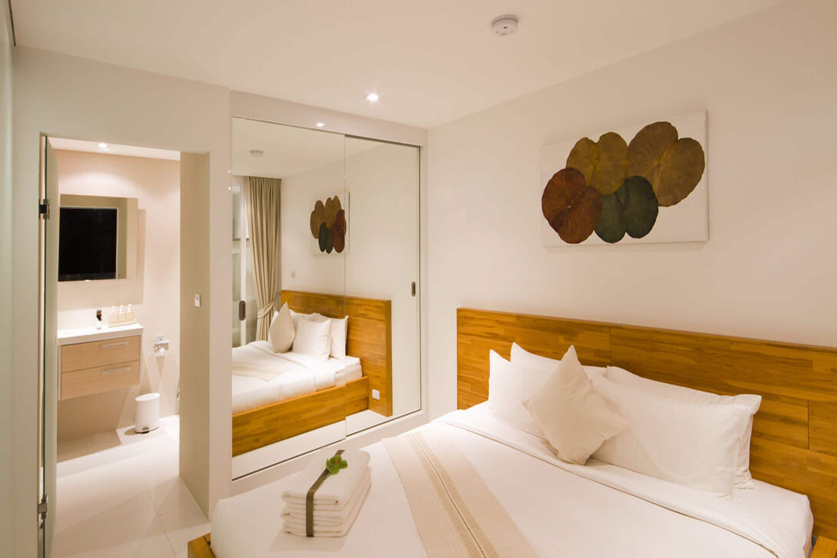 A modern hotel room with a large mirror, a wooden headboard, and a bed with white linens.