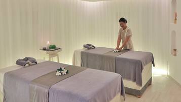 Un cuarto de spa con dos camillas, una mesita con una vela, y un estante en la pared.
