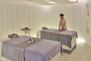 Un cuarto de spa con dos camillas, una mesita con una vela, y un estante en la pared.