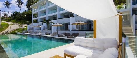 A poolside area with a white sofa, lounge chairs, and umbrellas.