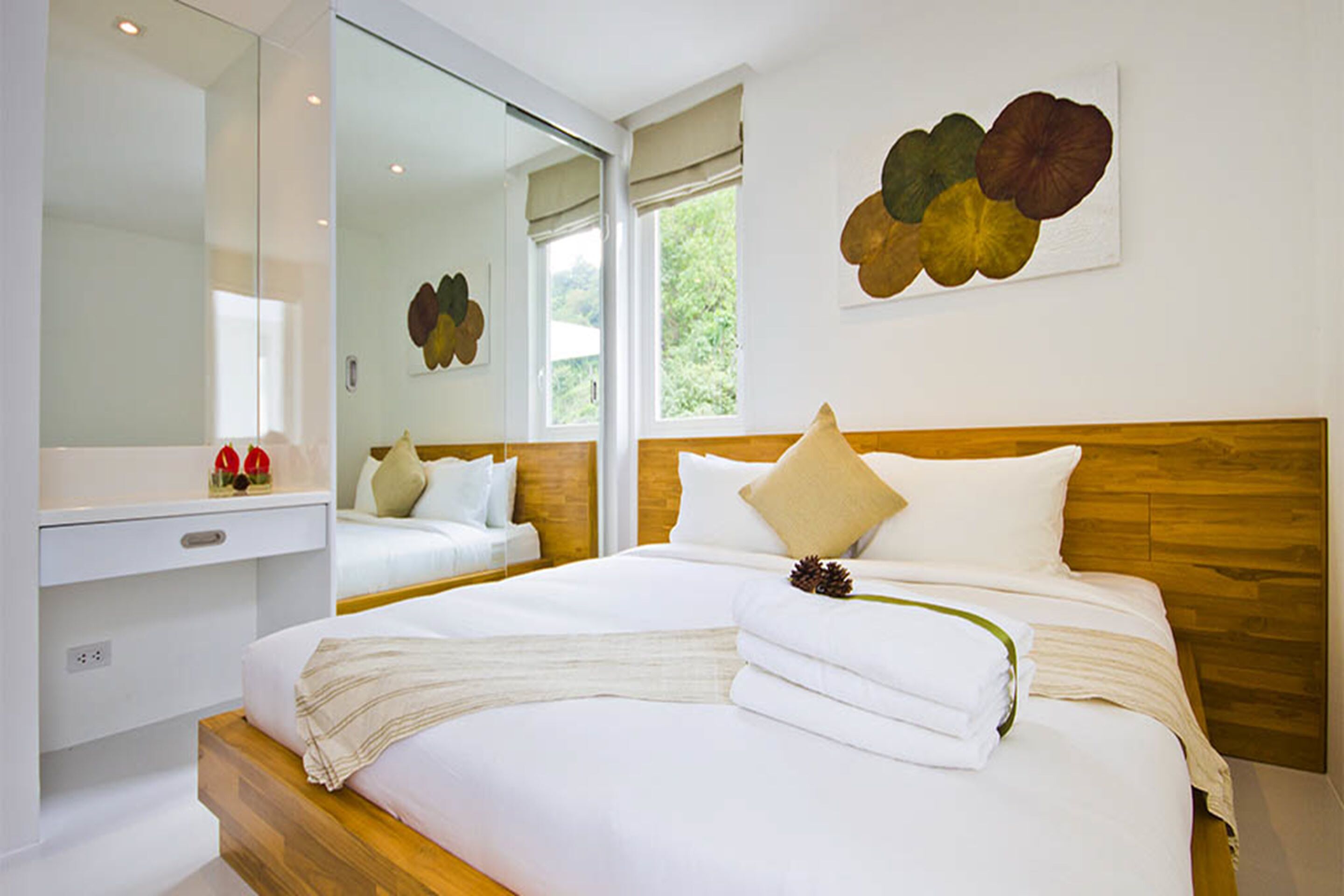 A modern hotel room with a large bed, a wooden headboard, a large mirror, and a window with a view of greenery.