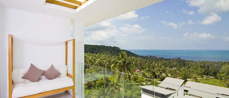 A modern room with a white sofa and a glass balcony overlooking a coastal landscape.