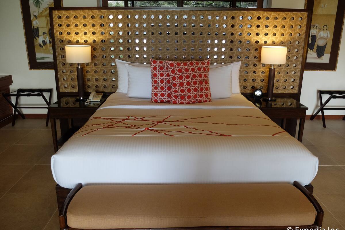 A hotel room with a large bed, two bedside lamps, a wooden headboard with circular cutouts, and artwork on the walls.