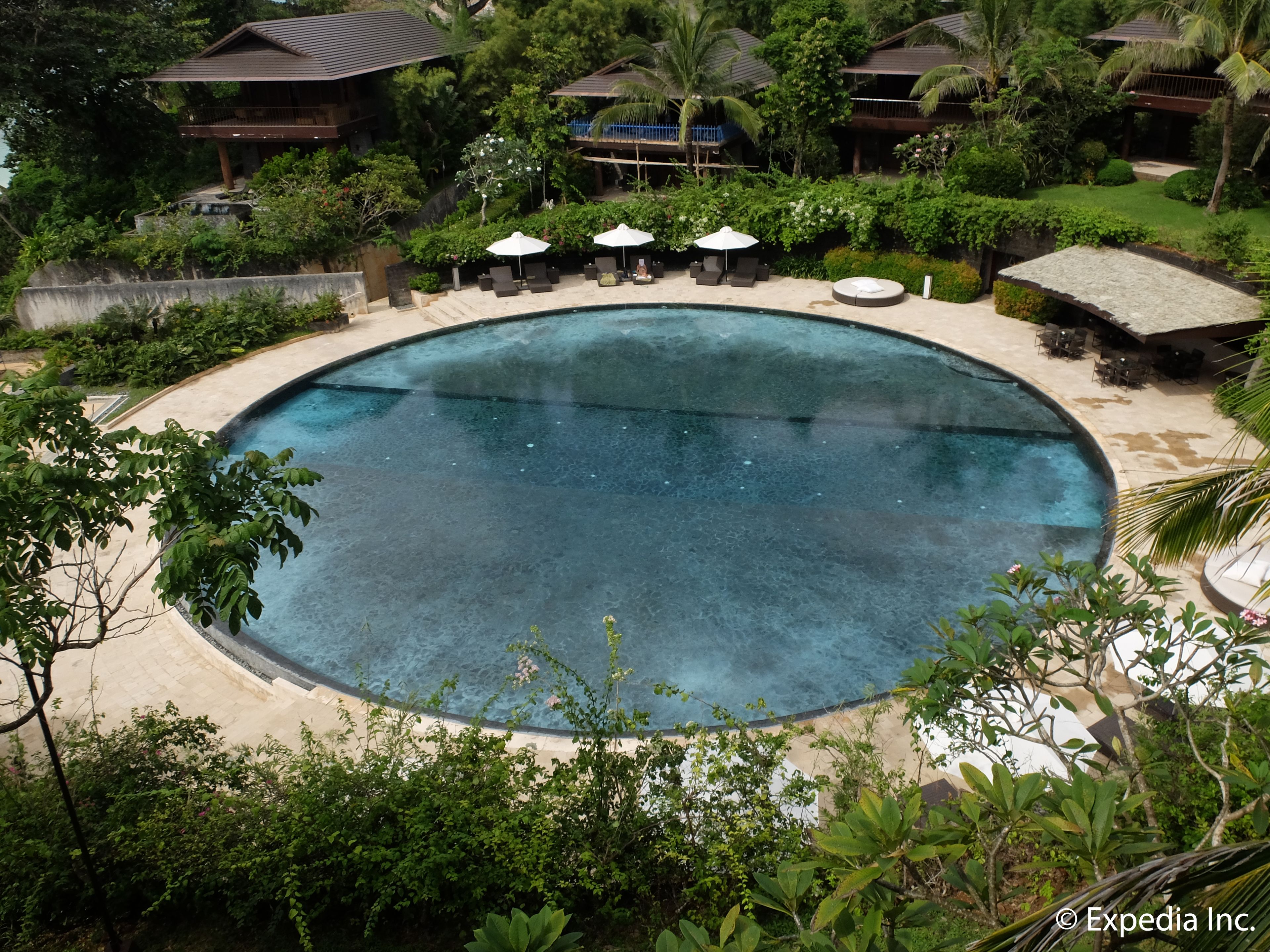 Une grande piscine circulaire, entourée de chaises longues et de parasols, avec une végétation luxuriante et les bâtiments du complexe hôtelier en arrière-plan.