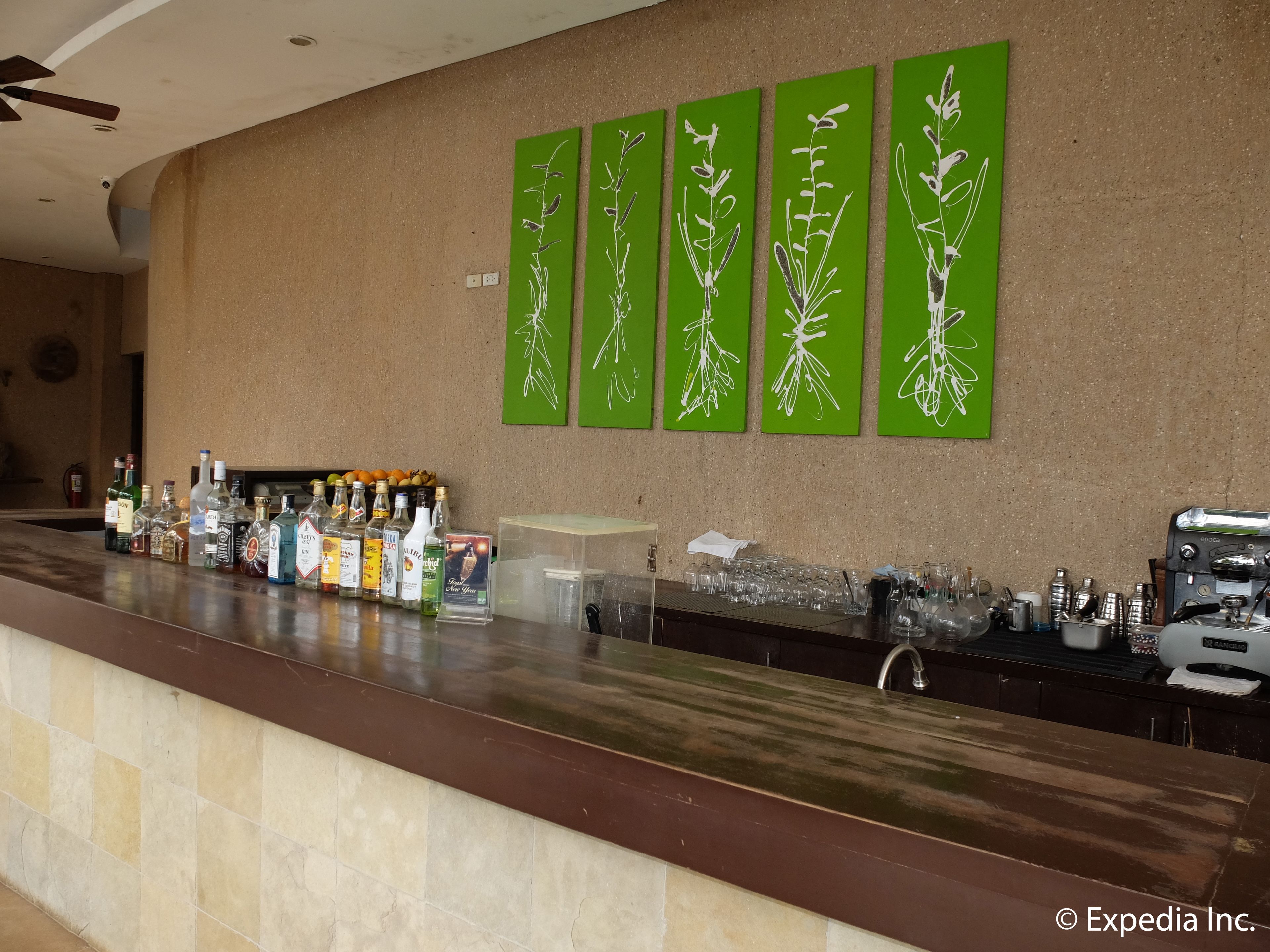 Uma área de bar com arte em parede verde, uma variedade de garrafas de bebidas e utensílios de bar.