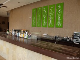 Uma área de bar com arte em parede verde, uma variedade de garrafas de bebidas e utensílios de bar.