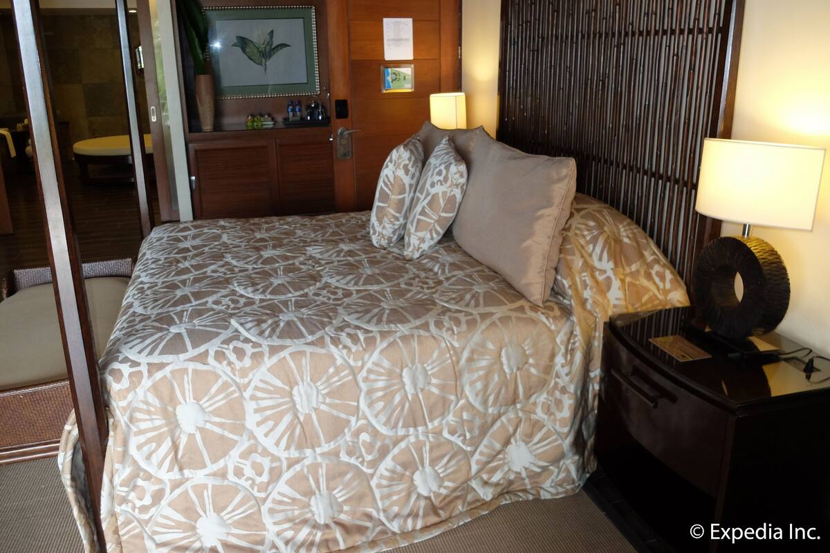 A hotel room with a bed, bedside lamps, a nightstand, a mirror, and a wooden panel wall.