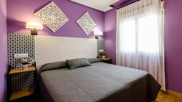 Une chambre avec un grand lit, deux tables de chevet, des motifs décoratifs sur les murs et une fenêtre avec des rideaux légers.