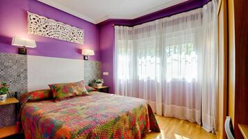 Une chambre à coucher avec une couvre-lit colorée à motifs matelassés, un panneau décoratif sur le mur et une grande fenêtre ornée de rideaux légers.