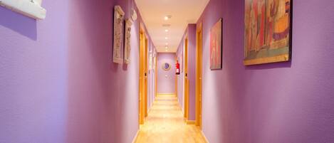 A long hallway with purple walls and wooden flooring, leading to a door at the end.