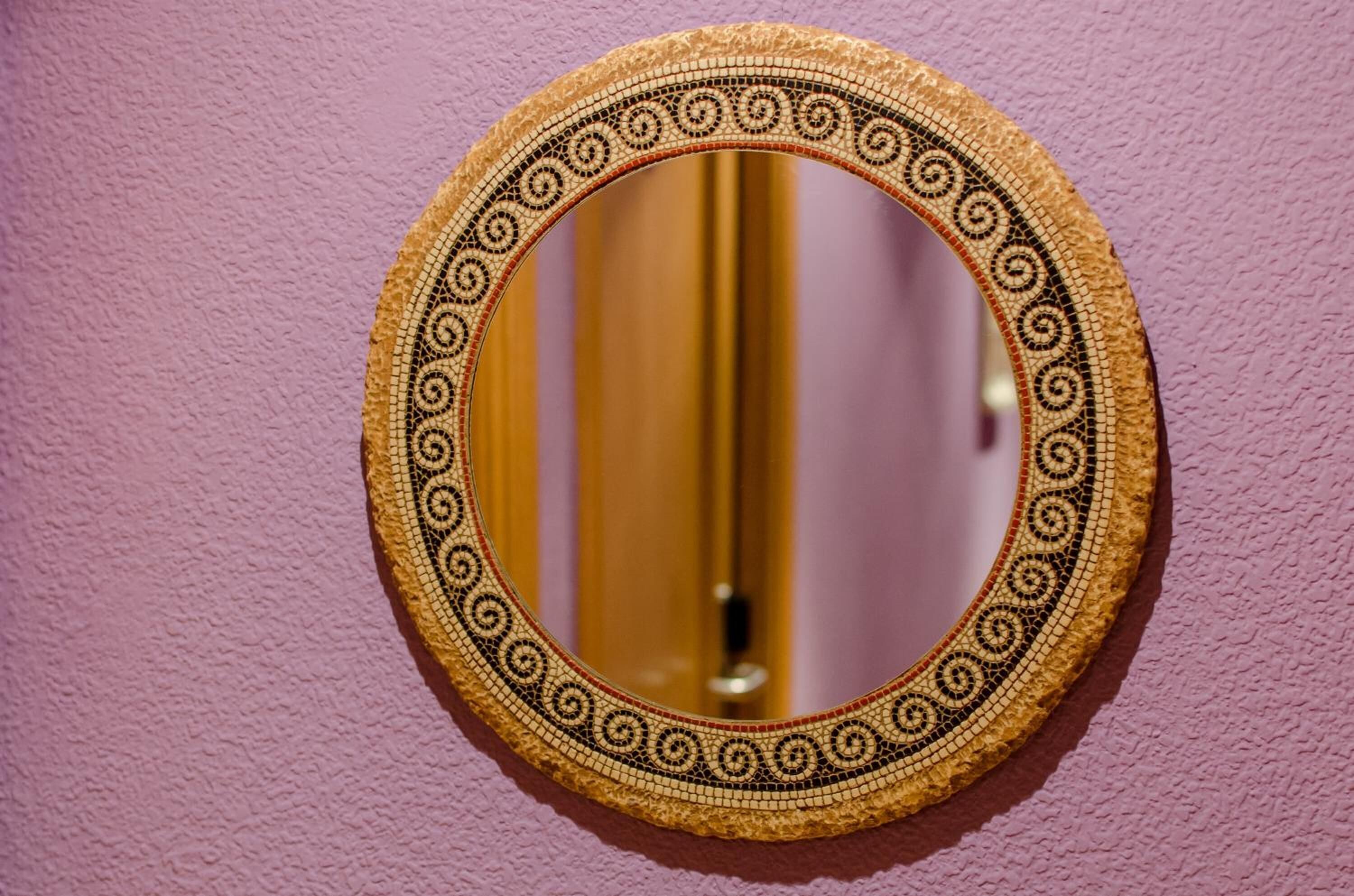 A round mirror with a decorative frame against a textured wall.