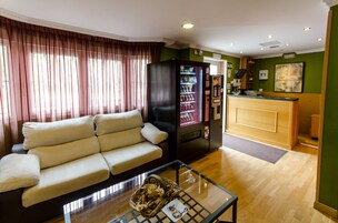 A hotel lobby with a sofa, a vending machine, a reception desk, and a framed artwork on the wall.