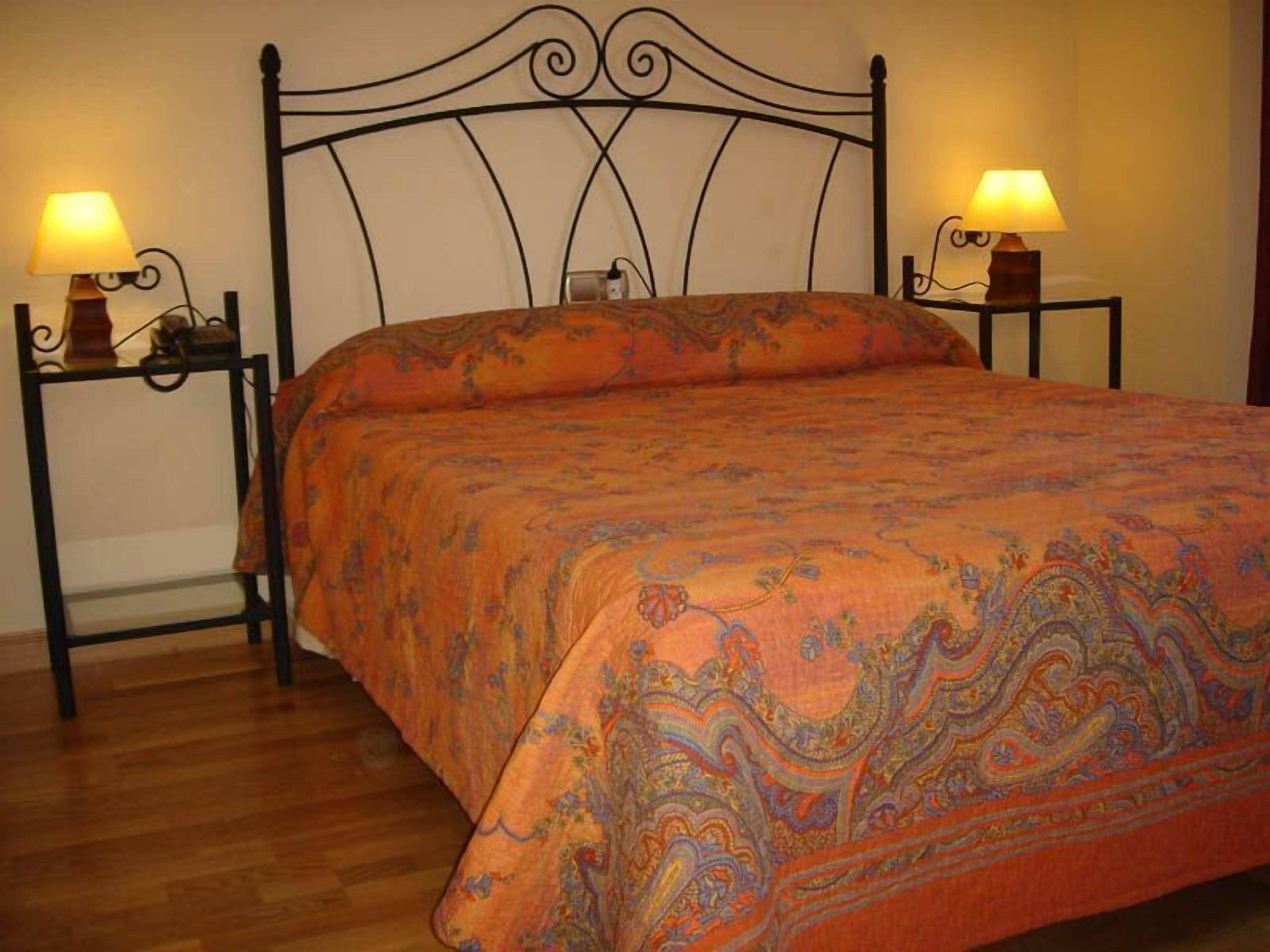A bed with an ornate headboard, two bedside tables with lamps, and a patterned bedspread.