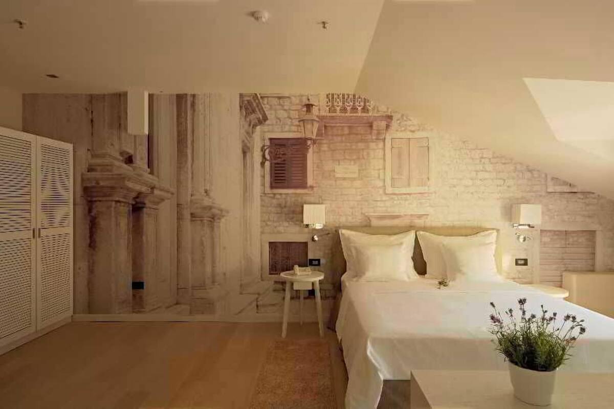 A bedroom with a bed, a nightstand, a wall-mounted lamp, and a small table.