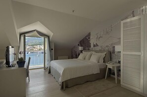 A bedroom with a large bed, a desk, a chair, and a view of a body of water through an open door.