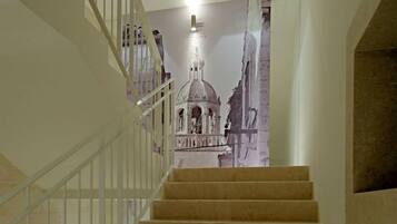 Una escalera con peldaños alfombrados en tono beige y barandillas blancas, que conduce a una habitación con un gran mural de un edificio histórico.