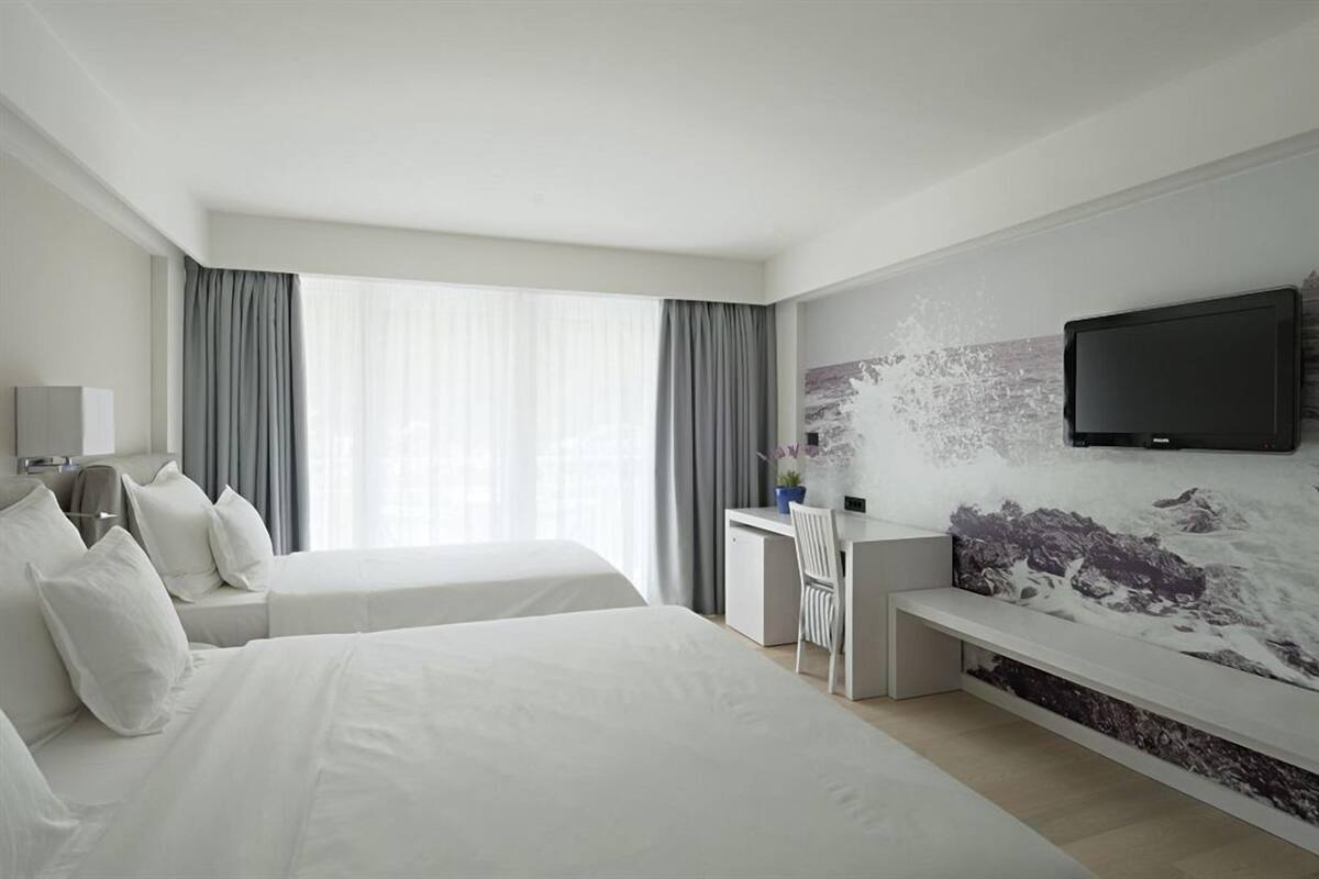 A modern hotel room with two beds, a desk, a flat-screen TV, and a large window with curtains.