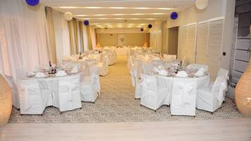 Een balzaal met ronde tafels gedekt voor een formeel evenement, met witte tafelkleden en stoelen, en een neutraal kleurenschema.