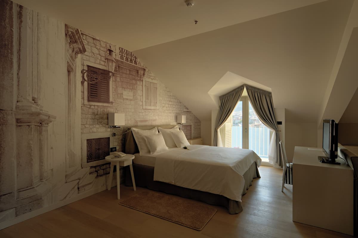 A bedroom with a stone wall, a bed, a desk, and a television.