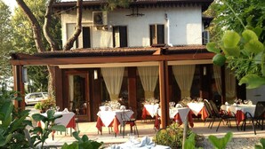 An outdoor dining area with tables set for guests, a covered seating area, and a building in the background. - Park Hotel Elefante (Verona)