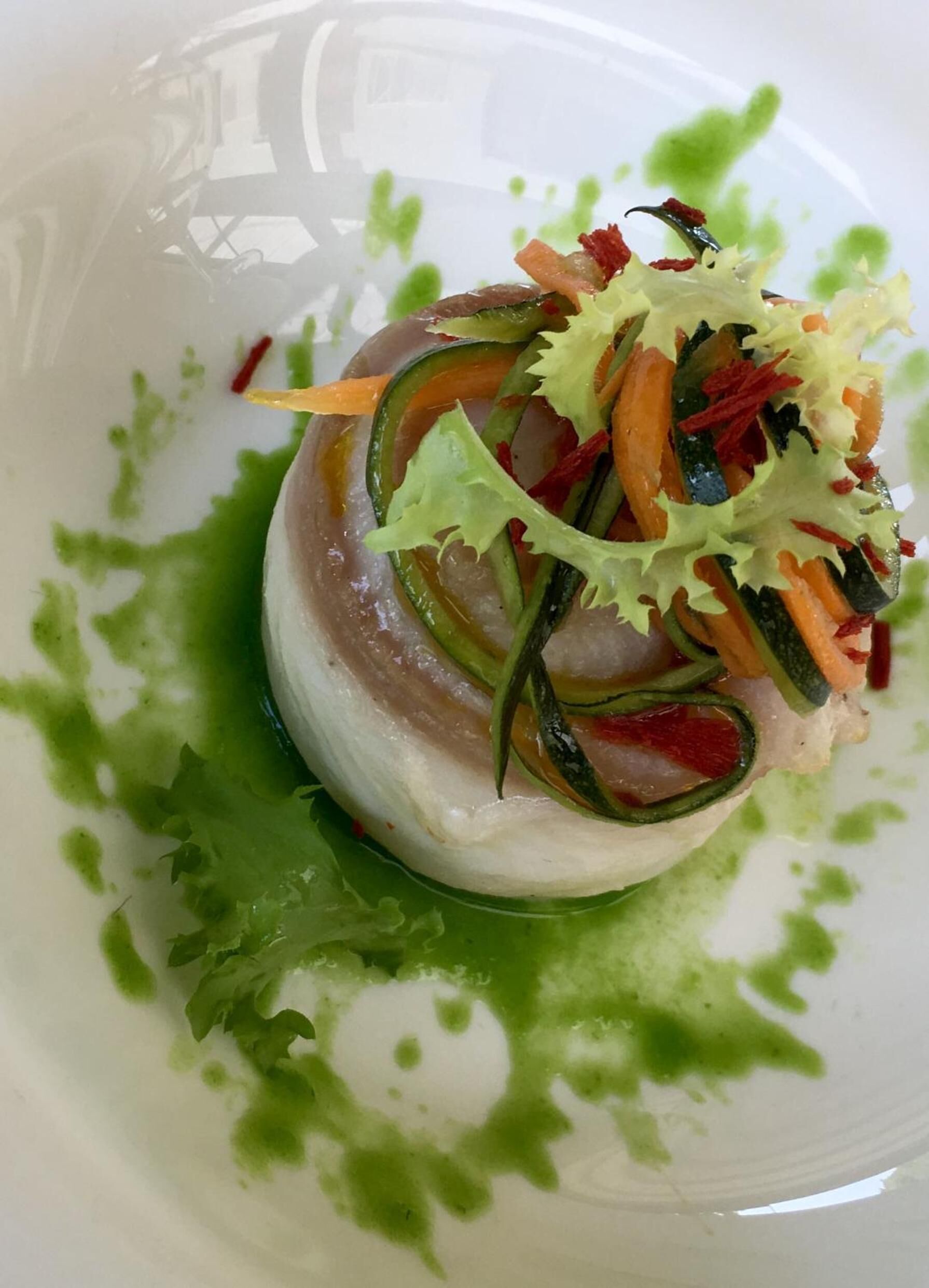Un plato con carne en lonchas finas, verduras y guarniciones sobre una vajilla blanca con salsa verde.
