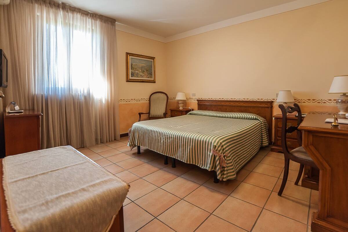 A hotel room with a bed, a desk, a chair, a TV, and a window with curtains.