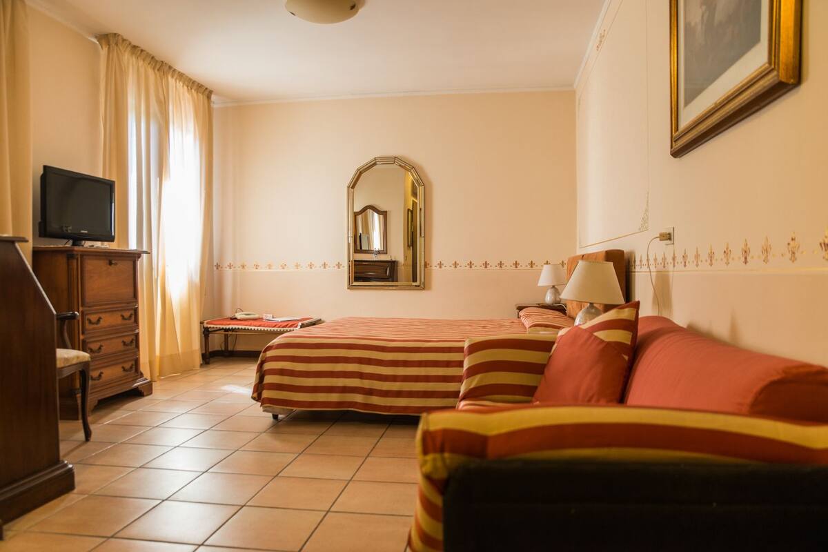 A hotel room with two beds, a television, a dresser, a mirror, and a lamp.