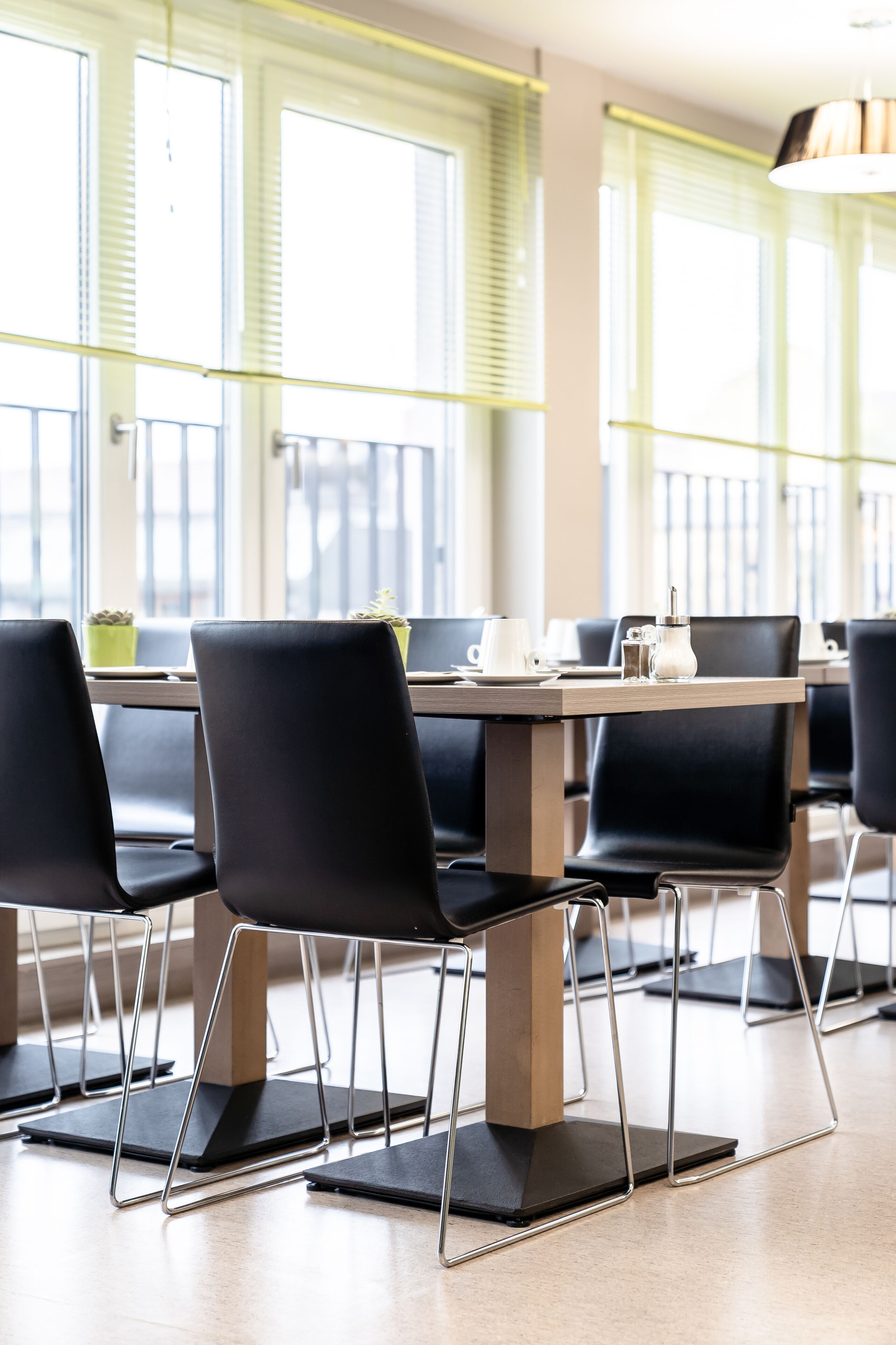 A modern dining area with black chairs, a wooden table, and a window with blinds.