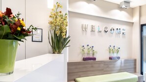 Una zona de recepción con un letrero que dice 'WELCOME', un banco verde y plantas en macetas.