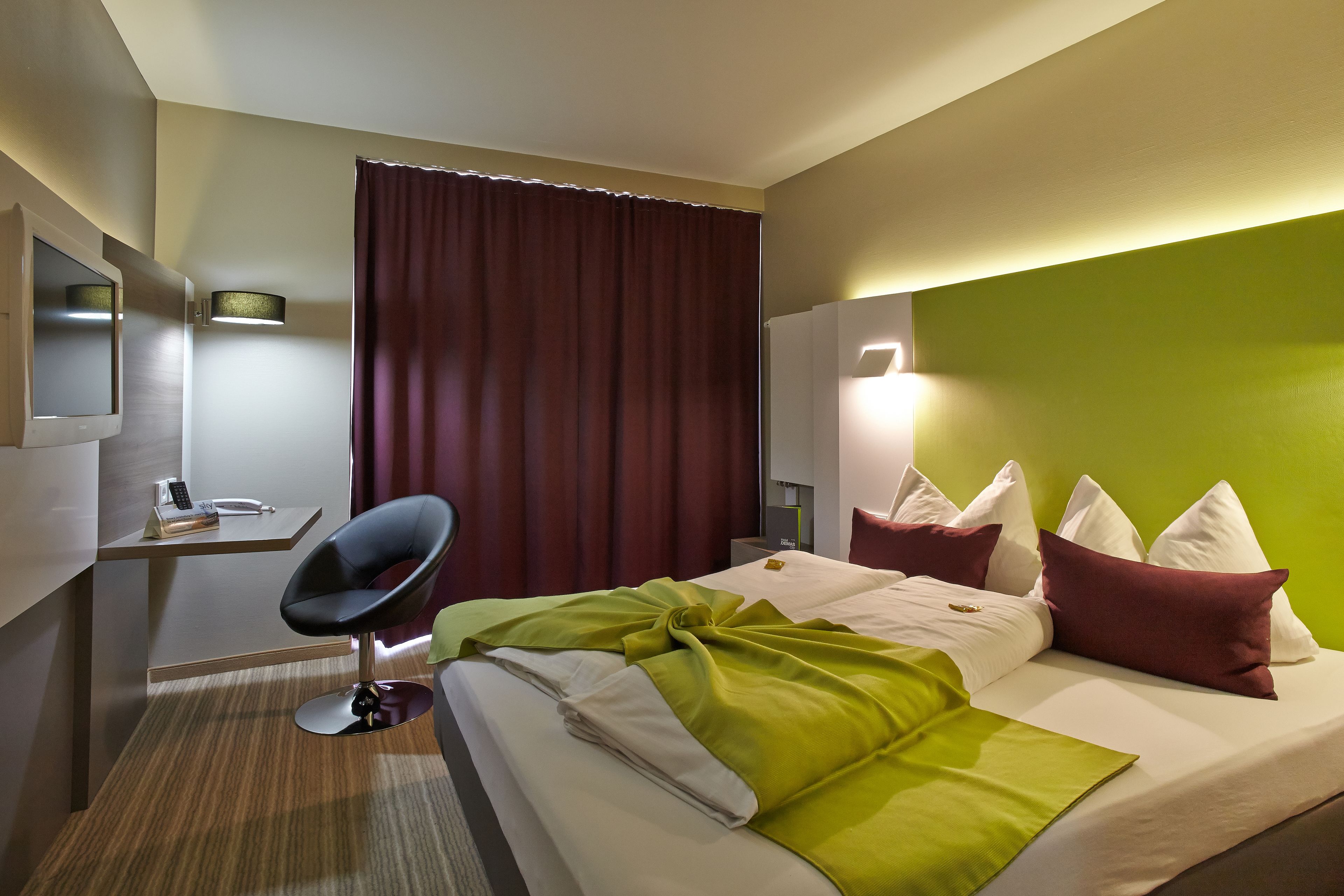 Una habitación de hotel con cama, escritorio, silla, espejo y cortina.