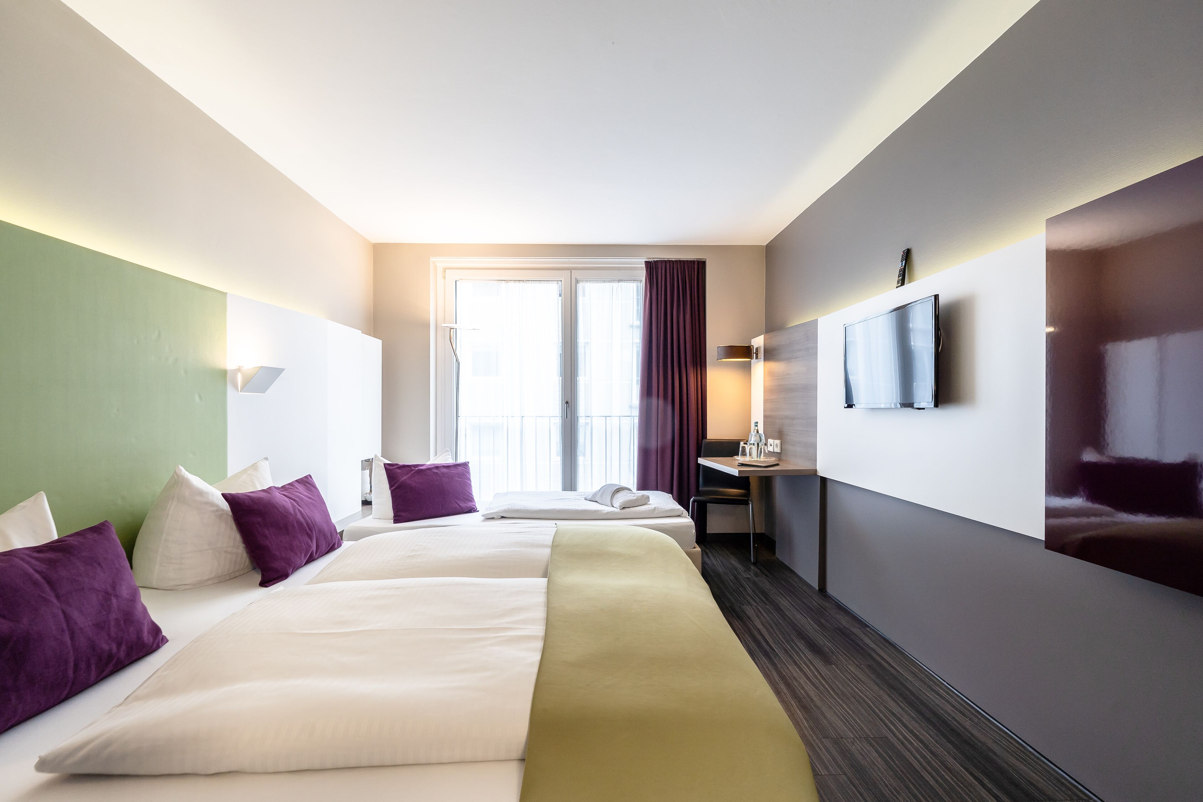 Habitación de hotel con dos camas, un escritorio, un televisor y una ventana con cortinas.