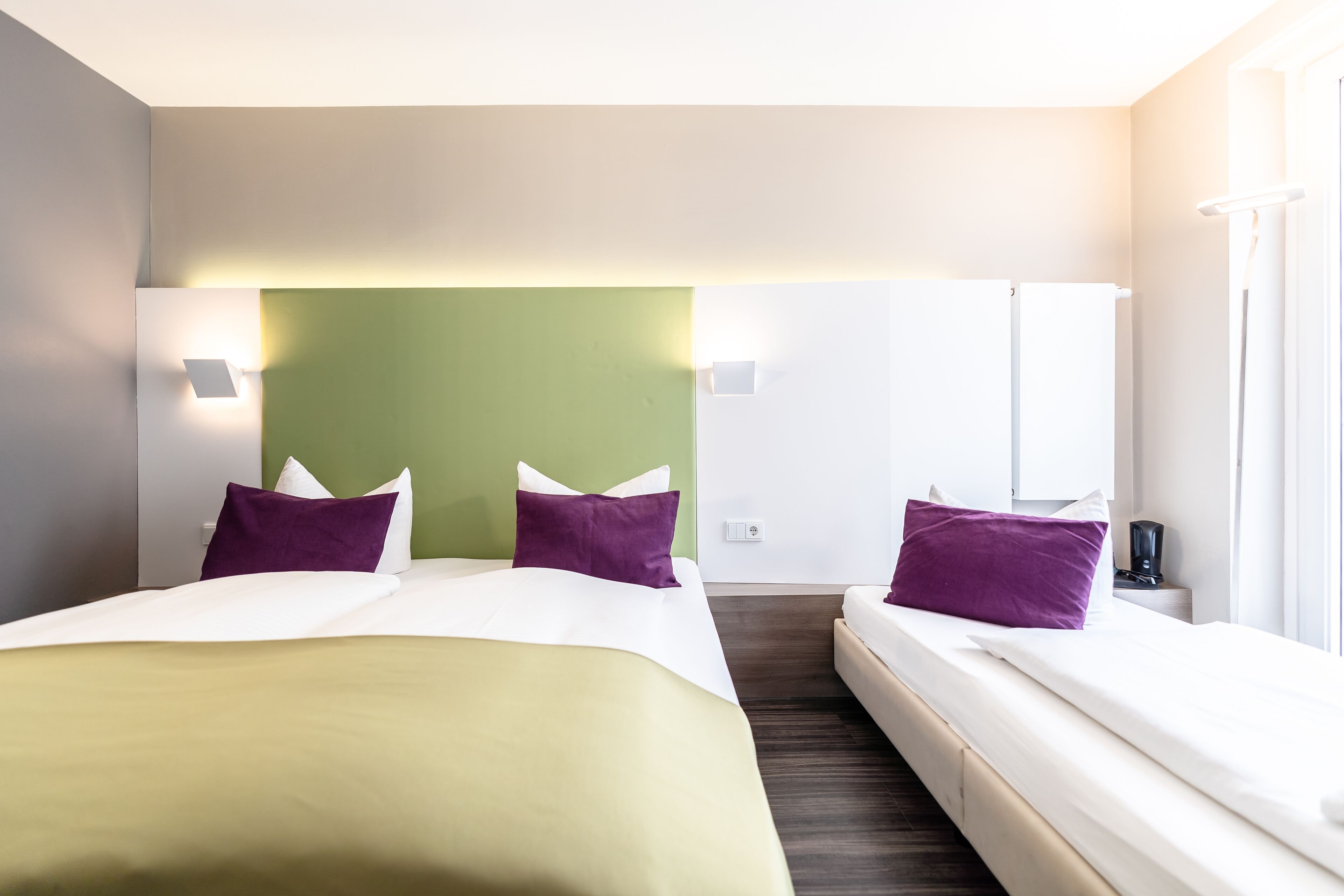 A hotel room with two beds, a green accent wall, and a white headboard.