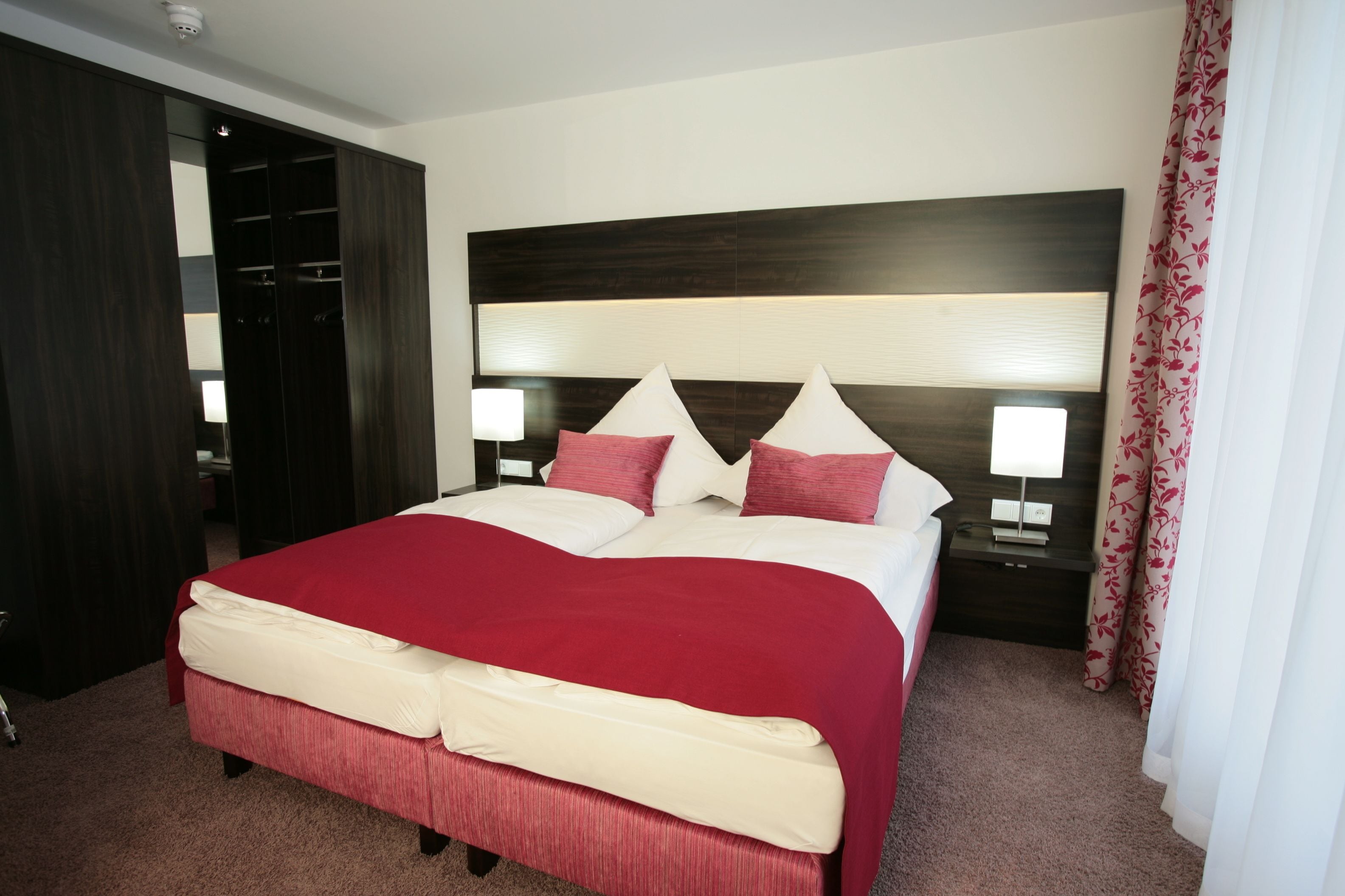 A hotel room with a large bed, two bedside tables, a wardrobe, and a nightstand with a lamp.