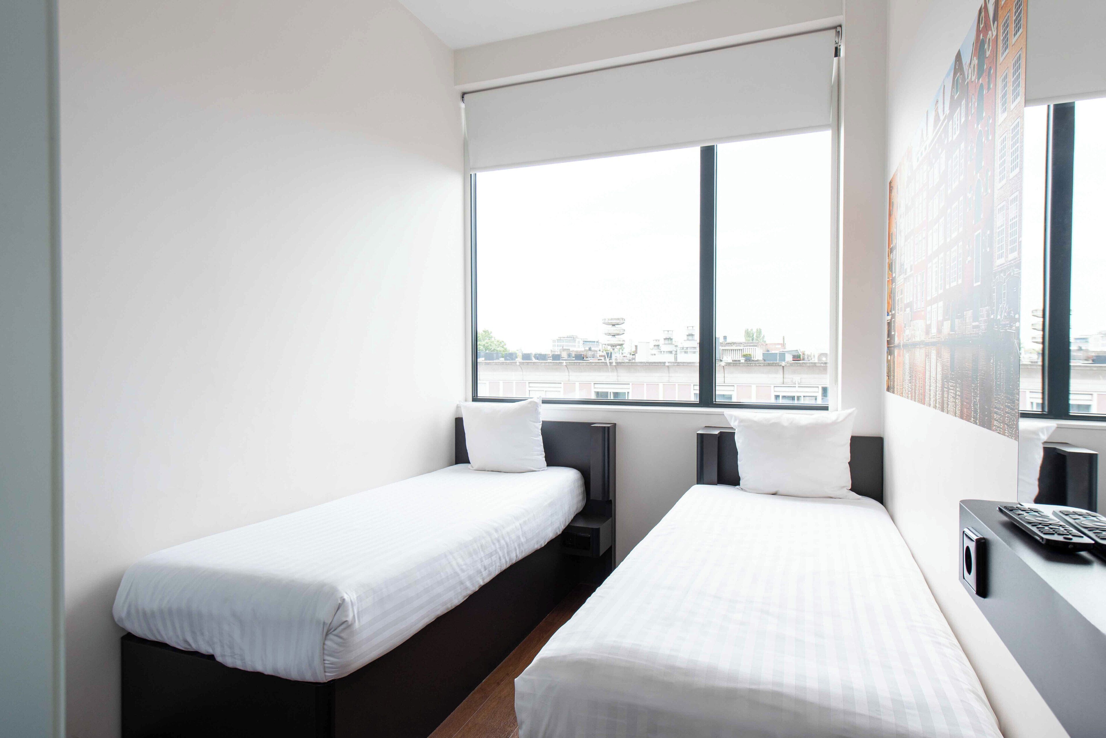 Una habitació d'hotel amb dos llits individuals, una finestra gran i vista a la ciutat.