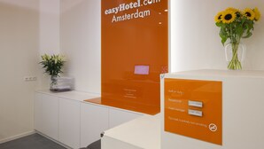 Una recepción con el letrero de easyHotel.com Ámsterdam, una planta y un jarrón con girasoles.