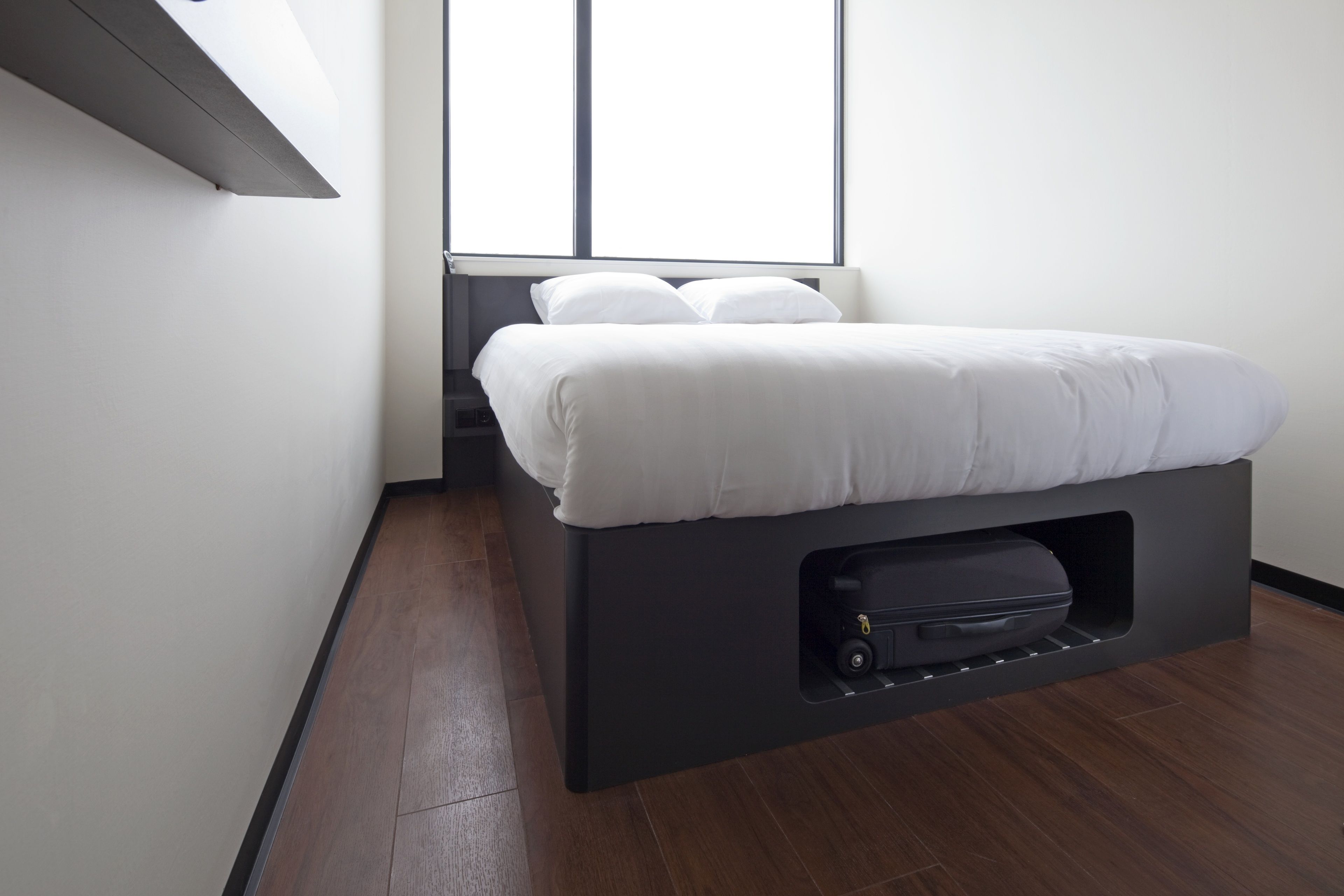 A modern room with a bed, a built-in storage unit below the bed, and a window providing natural light.