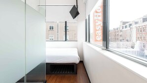 Una habitación moderna y compacta con cama, una lámpara colgante negra y una ventana con vista a la ciudad.