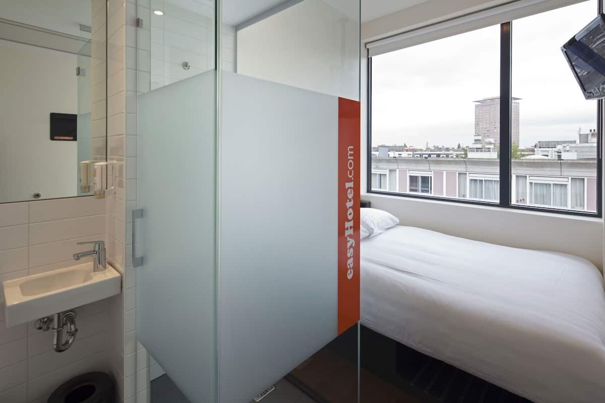 Una habitación de hotel con cama, ventana con vista a la ciudad, lavamanos y espejo.