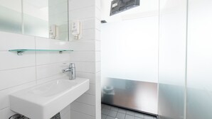 Un baño moderno con lavamanos, espejo y repisa de vidrio.