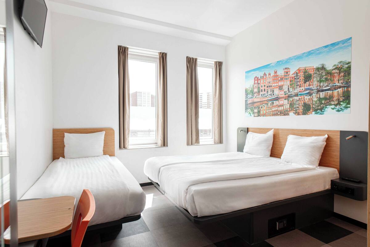 Habitación de hotel con dos camas, un escritorio, una silla, un televisor y un cuadro en la pared.
