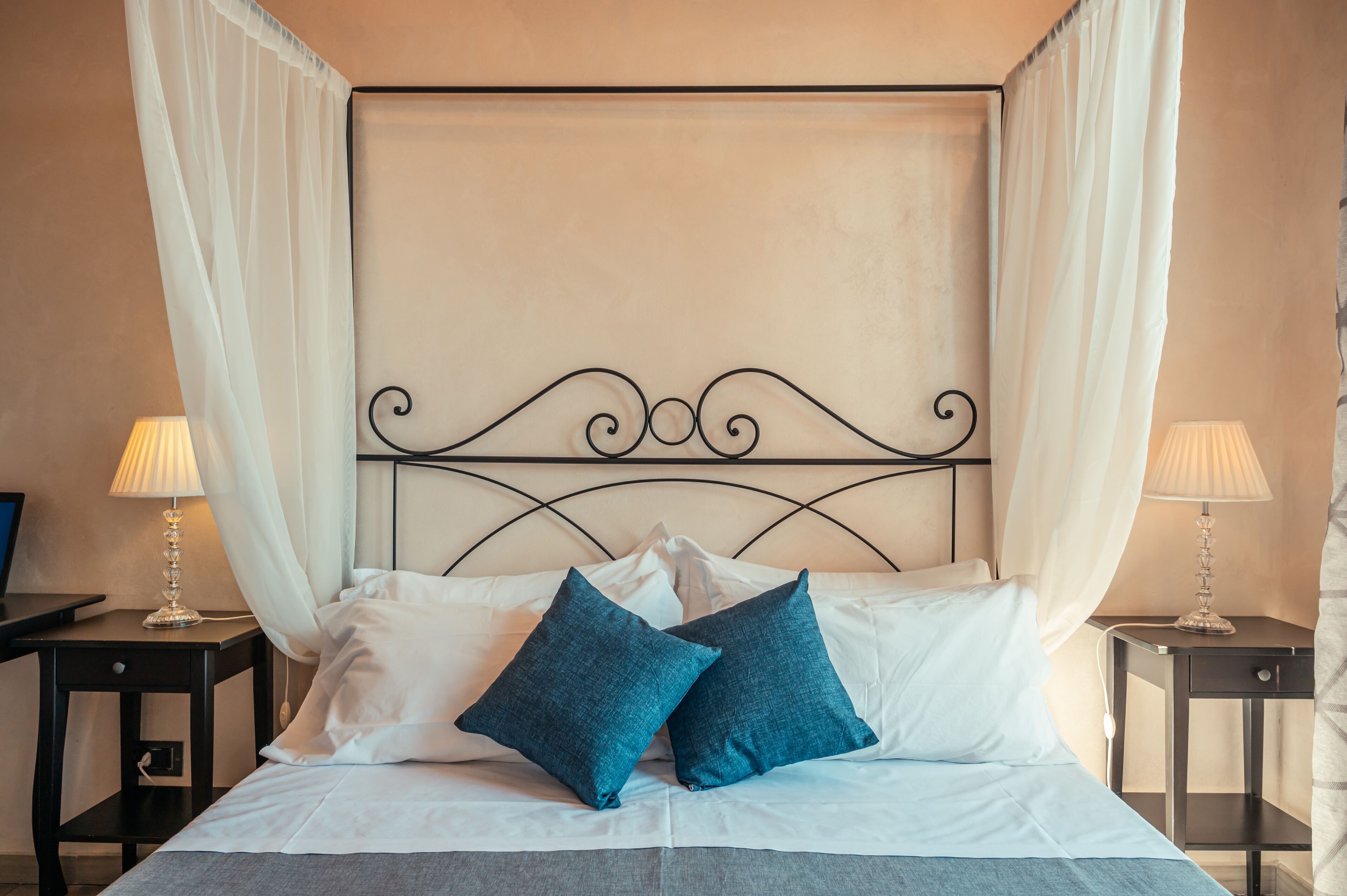 Een net opgemaakt bed met witte en blauwe kussens, een metalen hoofdbord en twee nachtkastjes met lampen.