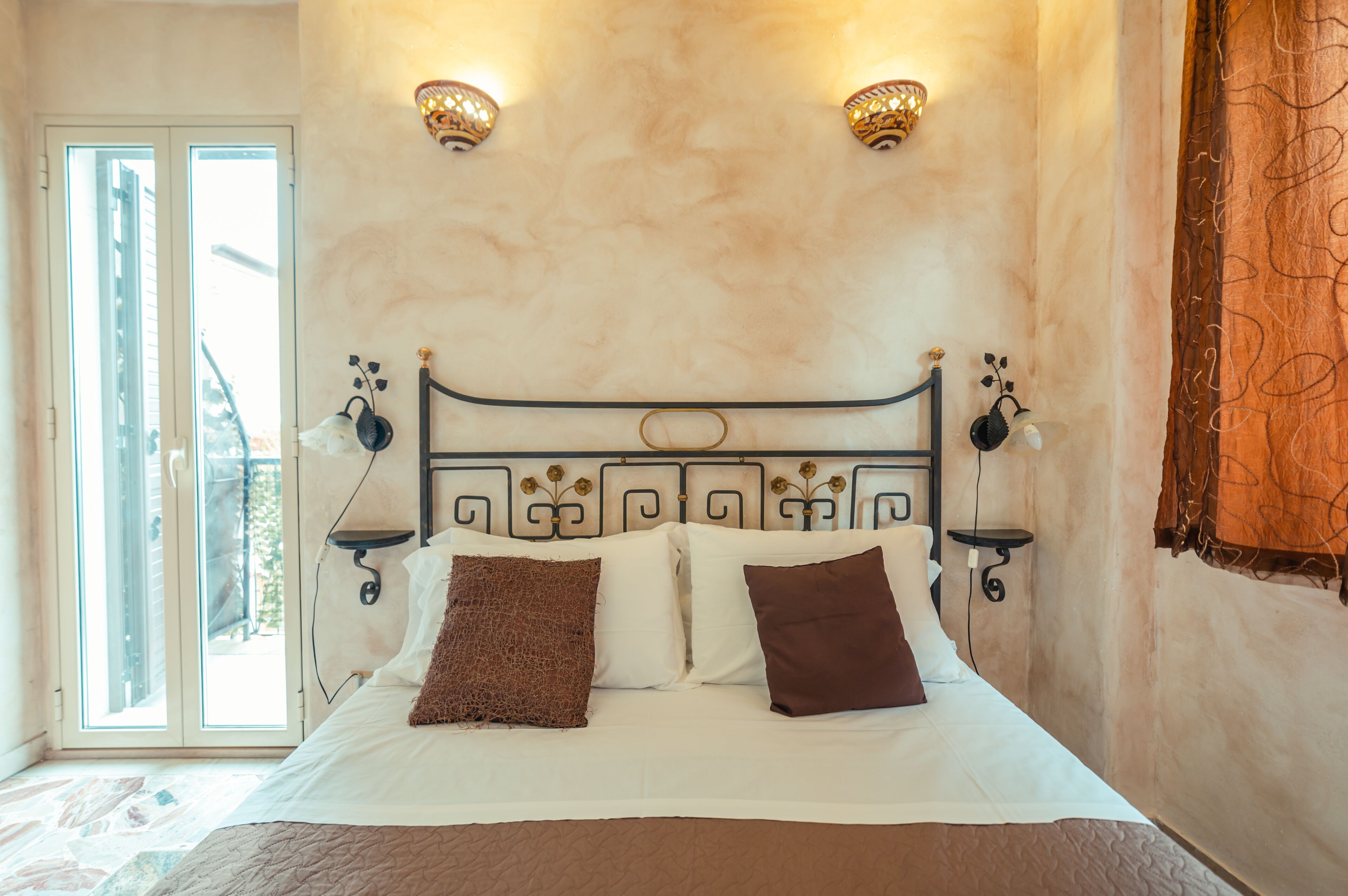 Un dormitorio con cama, dos apliques de pared, una ventana y una cortina.